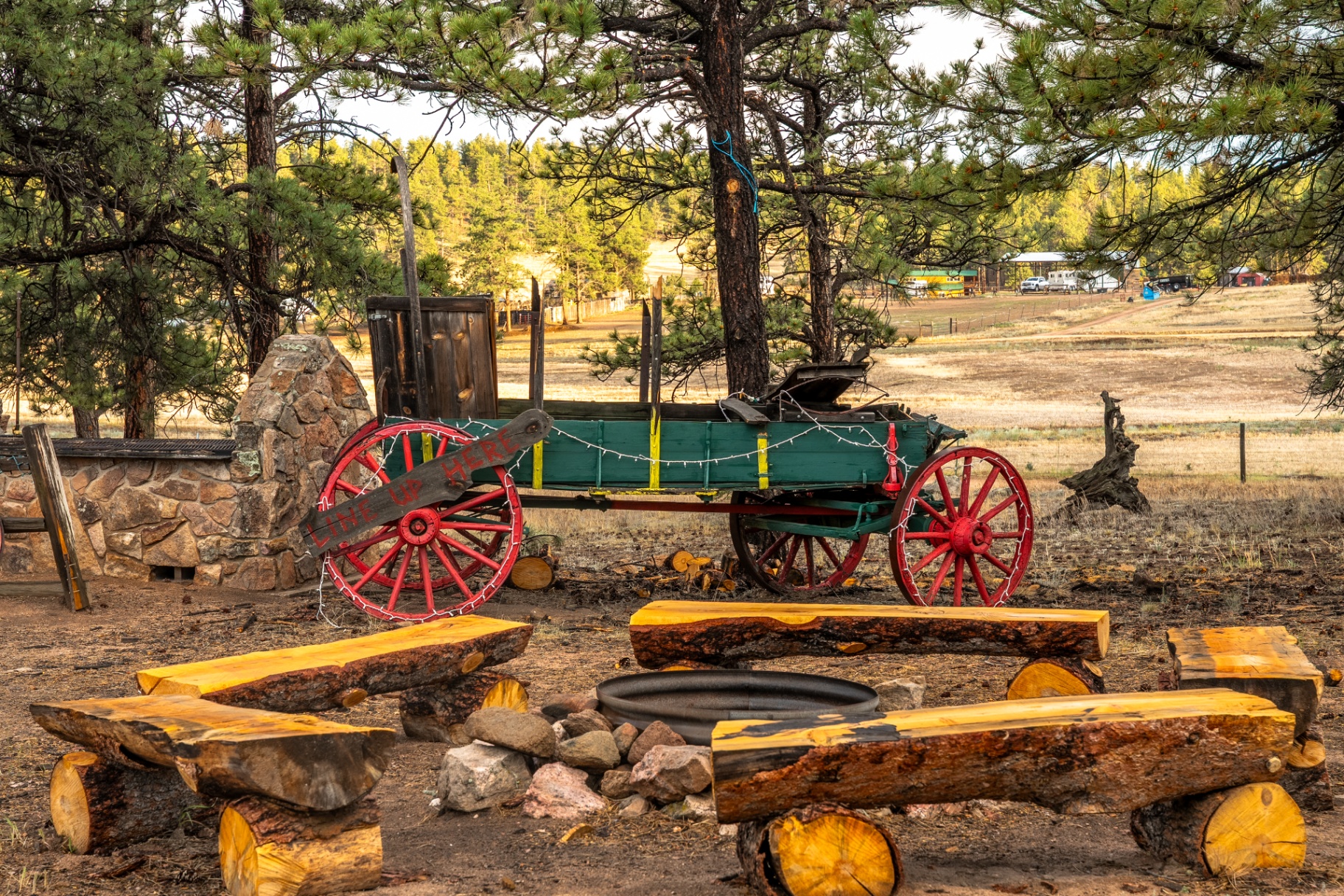 Rustic fire pit with log benches and a vintage wagon